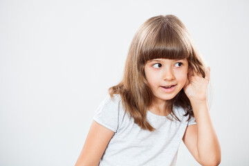 Studio shot portrait of thoughtful little girl who is eavesdropping. Copy space on gray background.