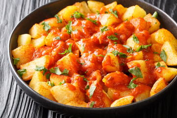 Spanish Crispy fried potatoes tossed in spicy brava sauce close up in the plate on the table. Horizontal
