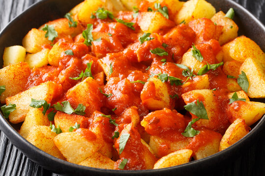 Spanish Patatas bravas it typically consists of white fried potatoes and served warm with a spicy sauce close up in the plate on the table. Horizontal