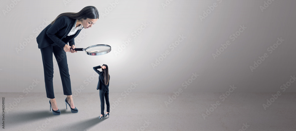 Poster Business woman in suit using magnifier magnifying glass to look at tiny subordinate on concrete background with shadow and mock up place. Hiring and dominance concept.