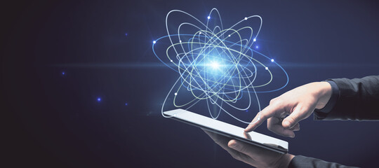 Close up of businessman hand holding pad with abstract glowing atom hologram on dark background. Science and connection concept.