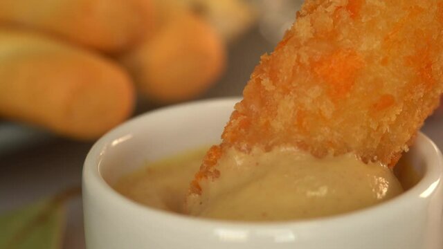 Breaded cheese stick dips in mustard. Deep fried crispbread snack with sauce. Food background. Extreme close up