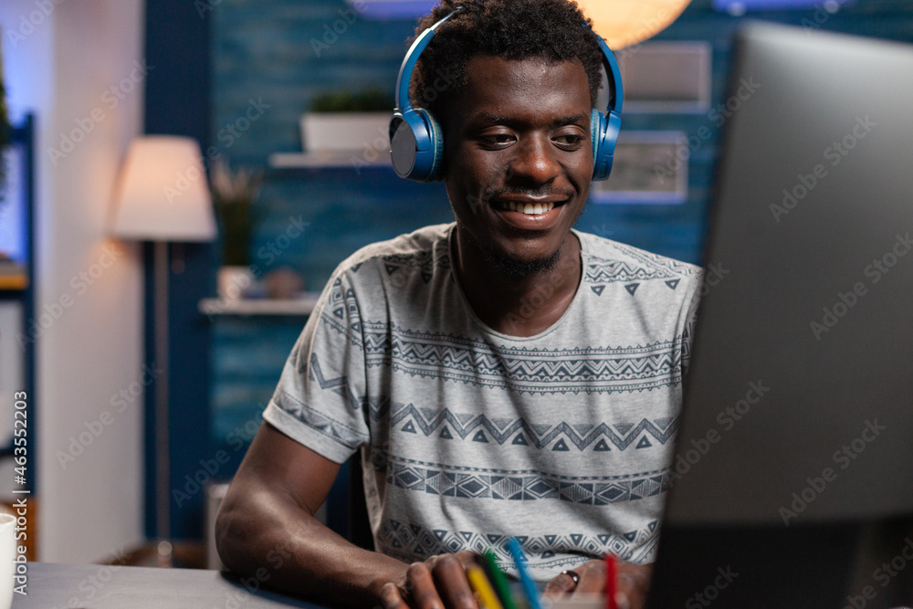 Poster smiling african american freelancer with headphones typing management ideas on computer working remo