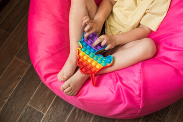 A little girl is playing with a modern pop it toy unicorn. A fascinating sensory toy for the development of hand motor skills. Colorful popit toy.Simple dimple. Baby's bare feet close up