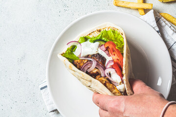Hand hold chicken gyros with vegetables, french fries and tzatziki sauce. Greek food concept.