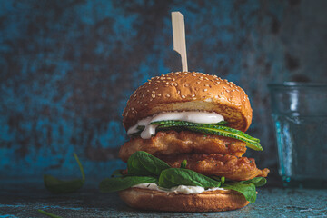 Fish burger on gray plate, dark blue background. Cod fish in batter with mayonnaise and spinach...
