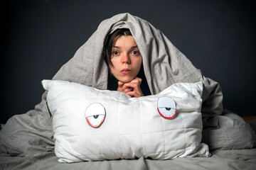 Cute sad young girl hugs a white pillow with painted eyes and face. 