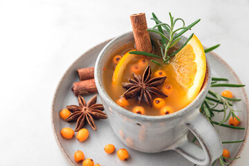 Cup of sea buckthorn tea with orange, berries, cinnamon and rosemary on white table. Close up
