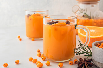 Sea buckthorn autumn tea with orange in glass cups and teapot with fresh berries, cinnamon and rosemary on white table