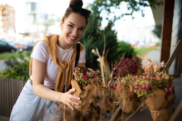 young beautiful brunette woman enjoying flowers in pots on the porch of a flower shop