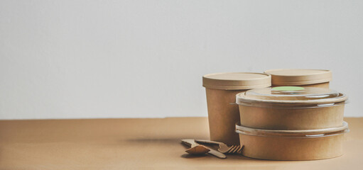 Selection of modern sustainable food delivery containers  and cutlery on kitchen table at white wall background. Front view with copy space. Banner