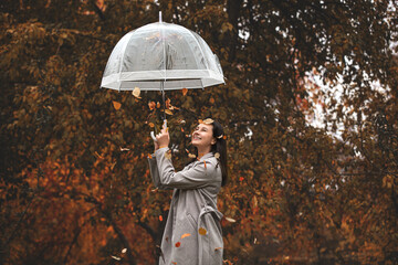 Beautiful happy young adult girl model, in autumn, walking in nature with an umbrella under a leaf...