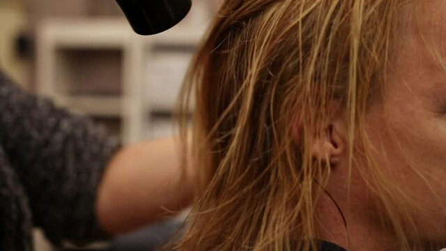A hairdresser blow-dries her client's freshly washed hair. She runs her hands through the hair to loosen it up.