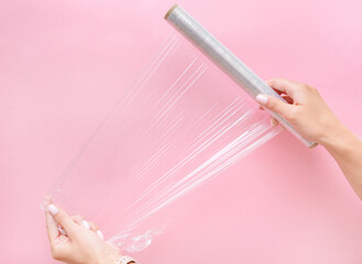 Two woman's hands holding plastic wrap on pink background