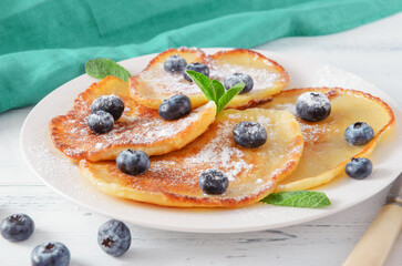 pancakes with blueberries, powdered sugar and mint on a plate, blue napkin on a white