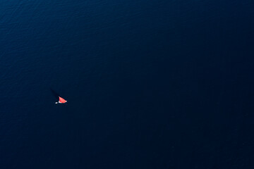 View from above, stunning aerial view of a sailboat with a red sail sailing on a blue water during a sunny day, Sardinia, Italy.
