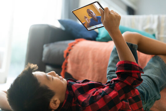 Smiling asian boy using tablet for video call, with elementary school pupil on screen