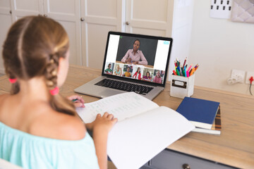 Caucasian girl using laptop for video call, with smiling diverse elementary school pupils on screen