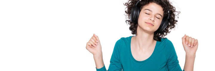 Fototapeta premium Young teenage girl wearing headphones listening and dancing to music isolated over white background. Happy girl enjoying a good song. Music concept.