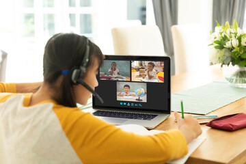 Asian girl using laptop for video call, with smiling diverse elementary school pupils on screen