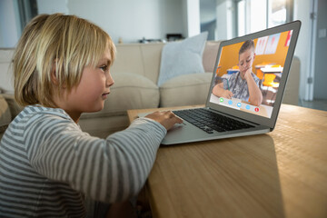 Caucasian boy using laptop for video call, with elementary school pupil on screen