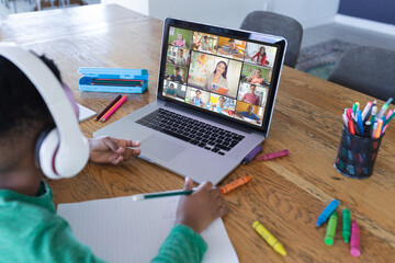 African american boy using laptop for video call, with diverse elementary school pupils on screen