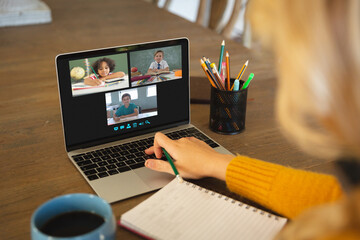 Fototapeta na wymiar Caucasian woman using laptop for video call, with smiling diverse elementary school pupils on screen