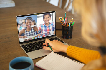 Fototapeta na wymiar Caucasian woman using laptop for video call, with smiling diverse high school pupils on screen