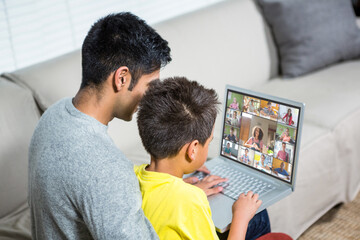 Biracial boy with father using laptop for video call, with elementary school pupils on screen