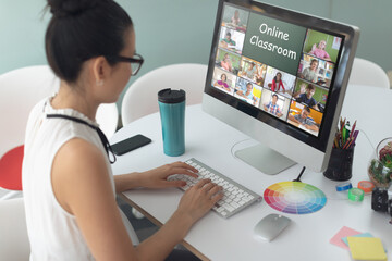 Asian girl using computer for video call, with smiling diverse elementary school pupils on screen