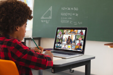 African american boy using laptop for video call, with diverse elementary school pupils on screen