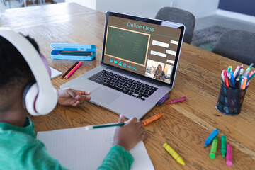 Fototapeta na wymiar African american boy using laptop for video call, with smiling female teacher on screen