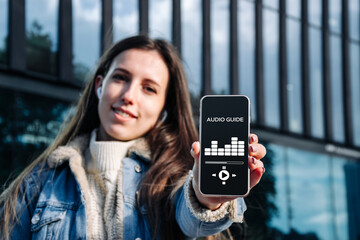 Audio tour online app on digital mobile smartphone. Happy young student woman holding phone listening audioguide. Simultaneous translation devices.