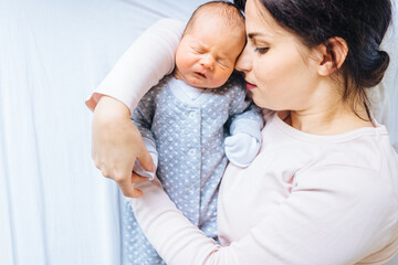 Middle age mother hugging with big love her newborn baby boy on bed at home. Beautiful conceptual image of Maternity. First moment of life.