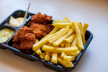 Dutch street food, portion of french fried potatoes, pieces of fried in oil cod fish fillet and two sauces