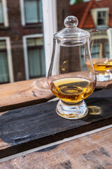 Dram of single malt scotch whisky served in tasting glass with view on old window and houses