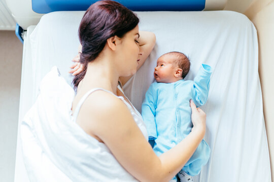 Top view portrait of a beautiful mother lying on bed, with her nursing baby in hospital. High quality photo. Love and tenderness, motherhood concept.