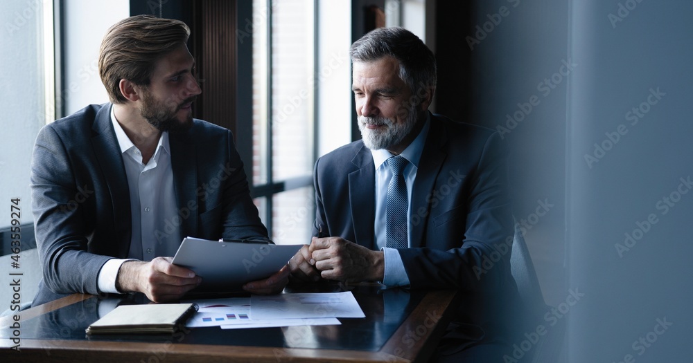 Sticker Senior and junior businessman discuss something during their meeting, office background.