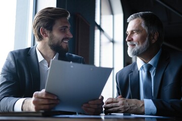Senior and junior businessman discuss something during their meeting, office background.