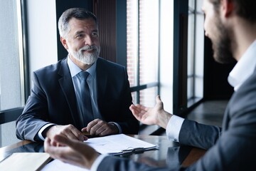 Senior and junior businessman discuss something during their meeting, office background.