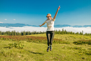 Fototapeta na wymiar Female tourist jumping up in the nature. Amazing Carpathians landscape background banner with hills, clouds and forest at dawn.