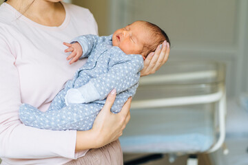 Mother holding newborn baby and calming down and rock to sleep little infant kid in hands at hospital. Love and tenderness, motherhood concept.