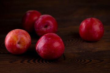 Red plum scattered on a wooden table, dark rustic photo