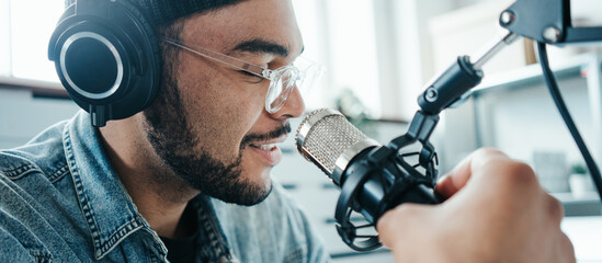 Cheerful mixed race content creator broadcasting his audio show at cozy home studio using...