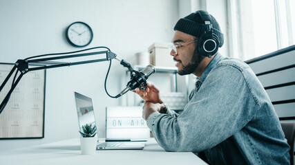 Mixed race content creator streaming his audio show at cozy home studio using professional microphone and laptop