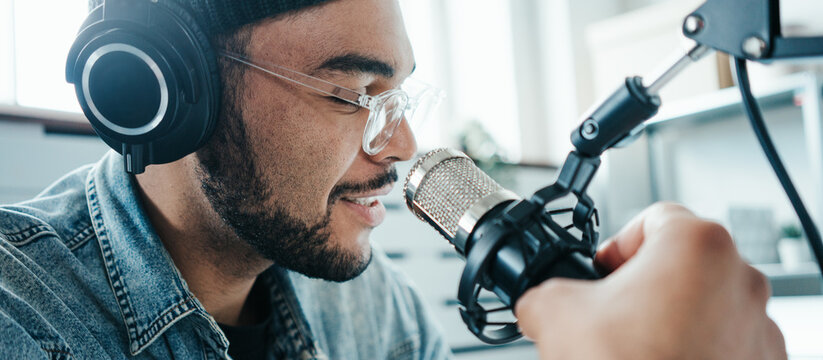 Cheerful mixed race content creator broadcasting his audio show at cozy home studio using professional microphone and laptop