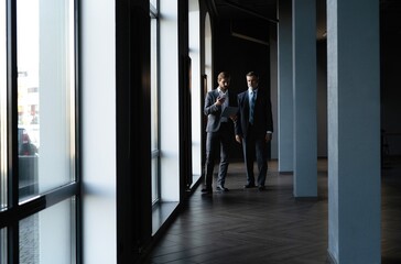 Two colleagues communicating in corridor, partners walking in the modern office