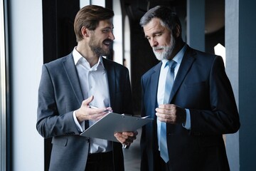 Two colleagues communicating in corridor, partners walking in the modern office