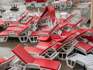 Heap of white plastic chaise lounge with red mattresses and sunshades on sea side cement beach top view