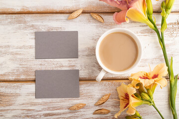 Obraz na płótnie Canvas Gray paper business card mockup with orange day-lily flower and cup of coffee on white wooden background. top view, copy space.